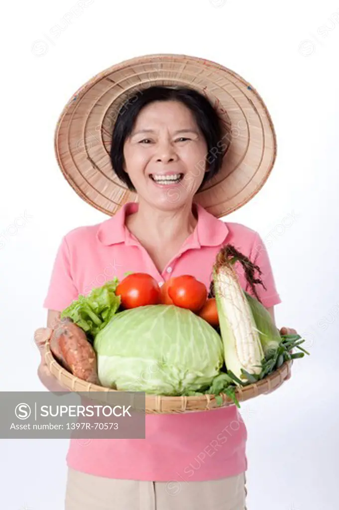Mature farmer holding a sieve of vegetables, laughing