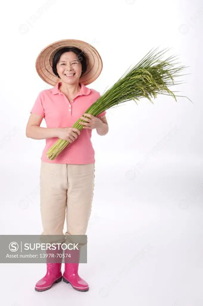 Mature farmer standing and holding rice plants, smiling