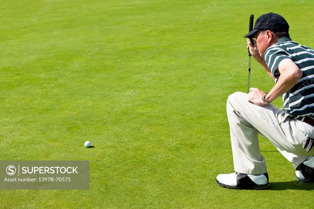 Man crouching on the lawn and looking at the golf ball