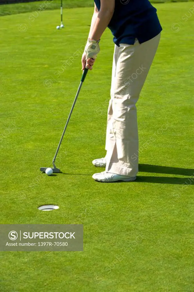 Woman standing on the lawn and putting with golf swing
