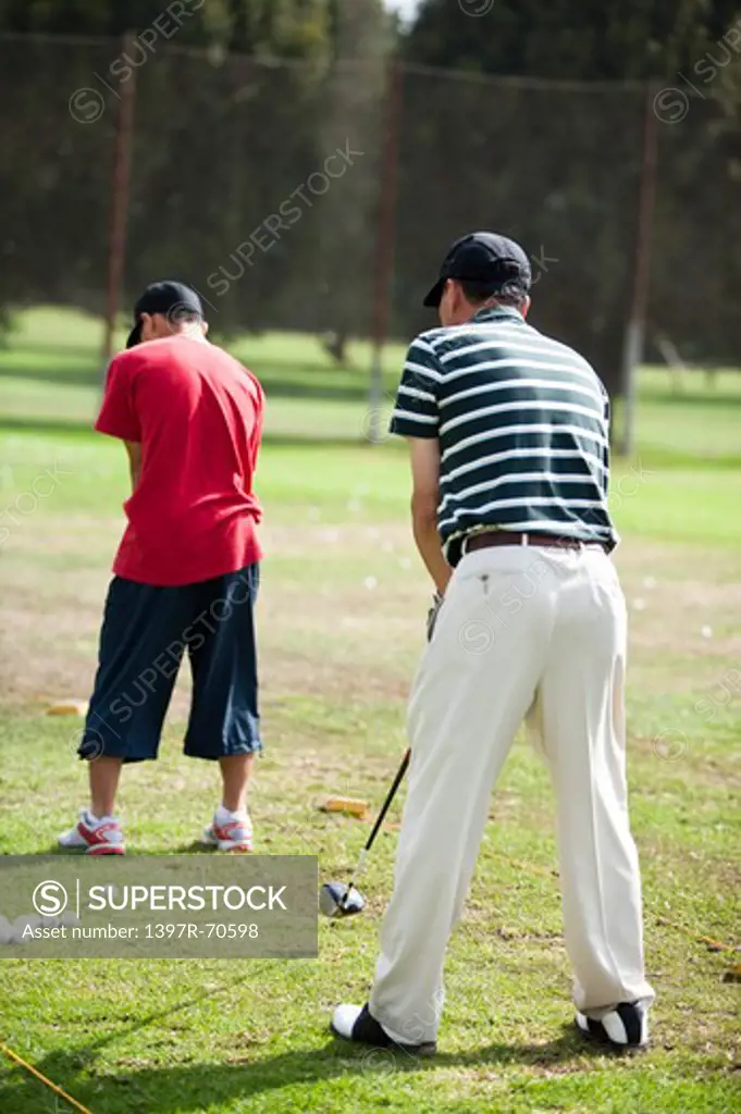 Father and son holding golf swing and standing on the lawn together