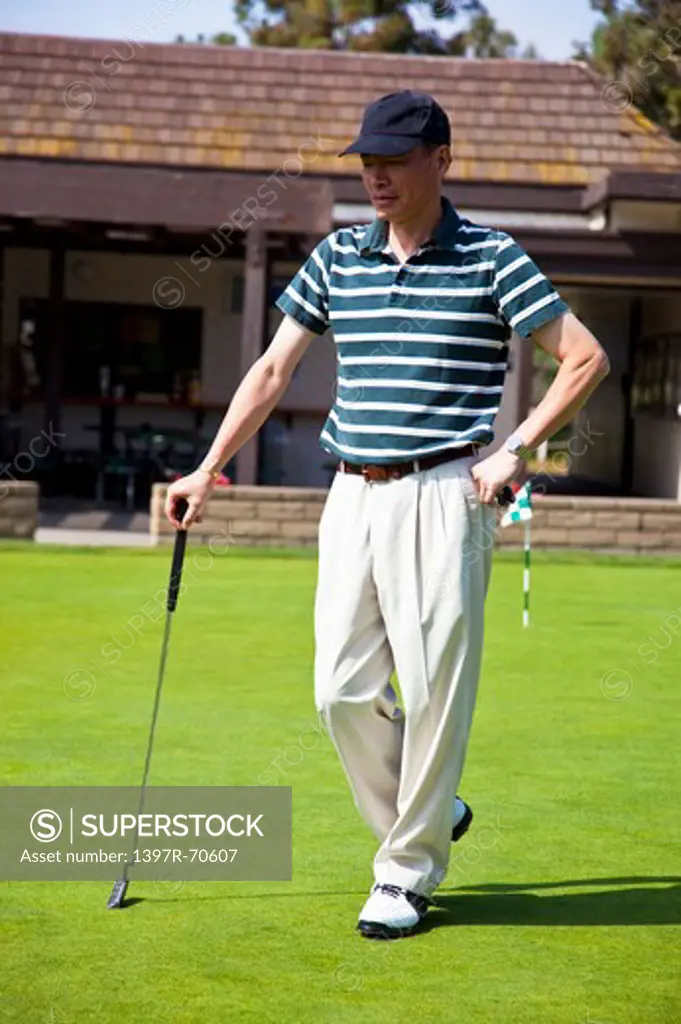 Man holding golf swing, standing on the lawn and looking down