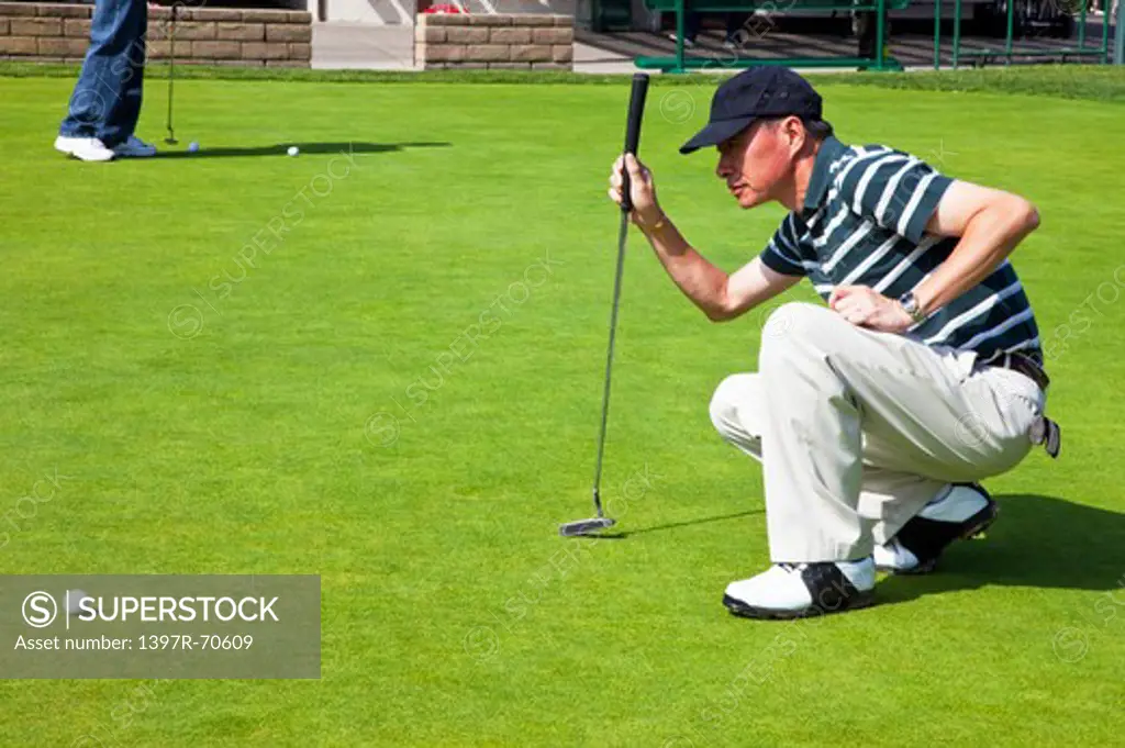 Man crouching on the lawn and putting with golf swing