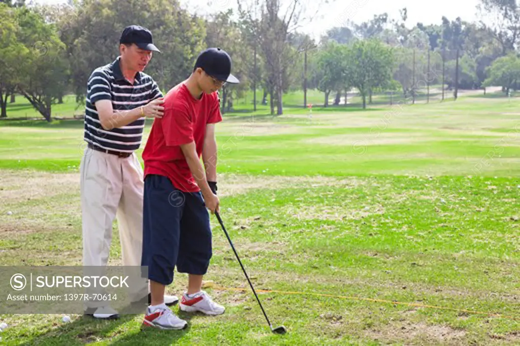 Man teaching teenager boy golf