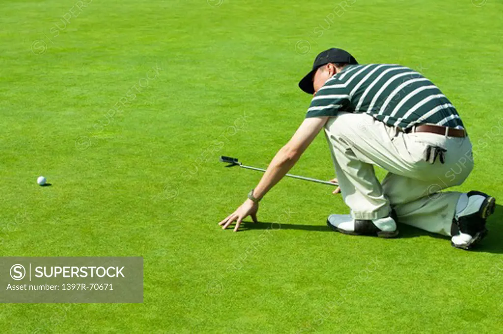 Man kneeling on the green lawn and looking at the golf ball