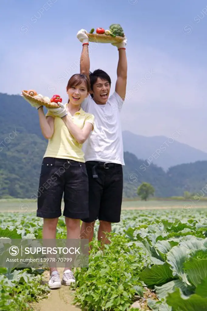Young couple holding vegetables in the vegetable garden and smiling happily