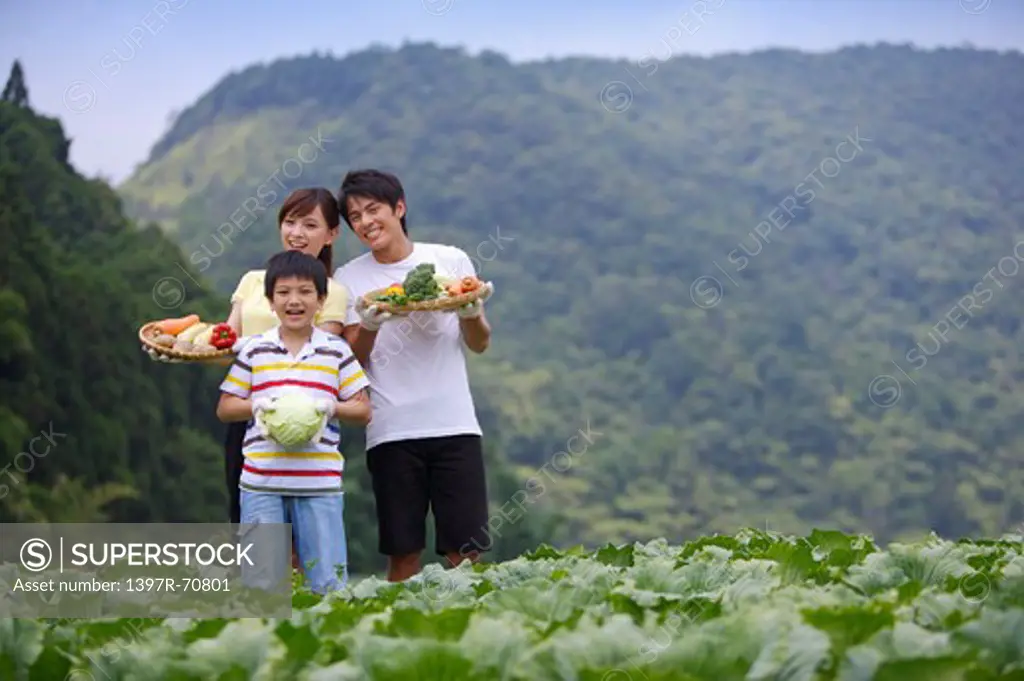 Young family with one child holding vegetables in the vegetable garden and smiling
