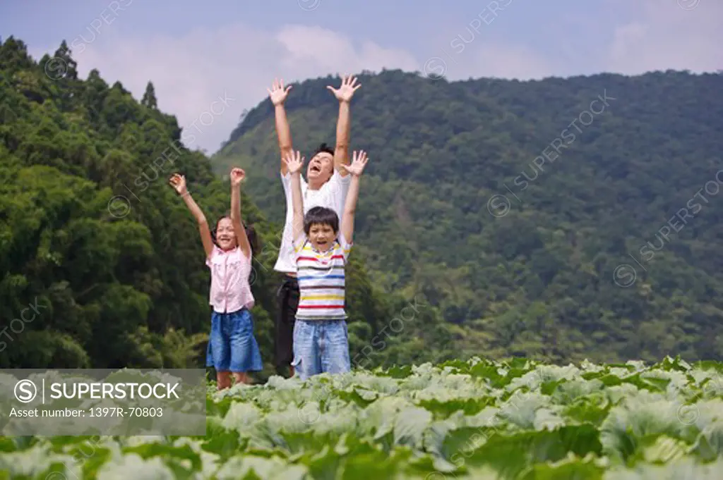 Young man with two children standing in the vegetable garden with arms outstretched