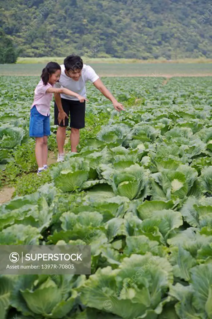 Young man with one child standing in the vegetable garden and pointing with smile