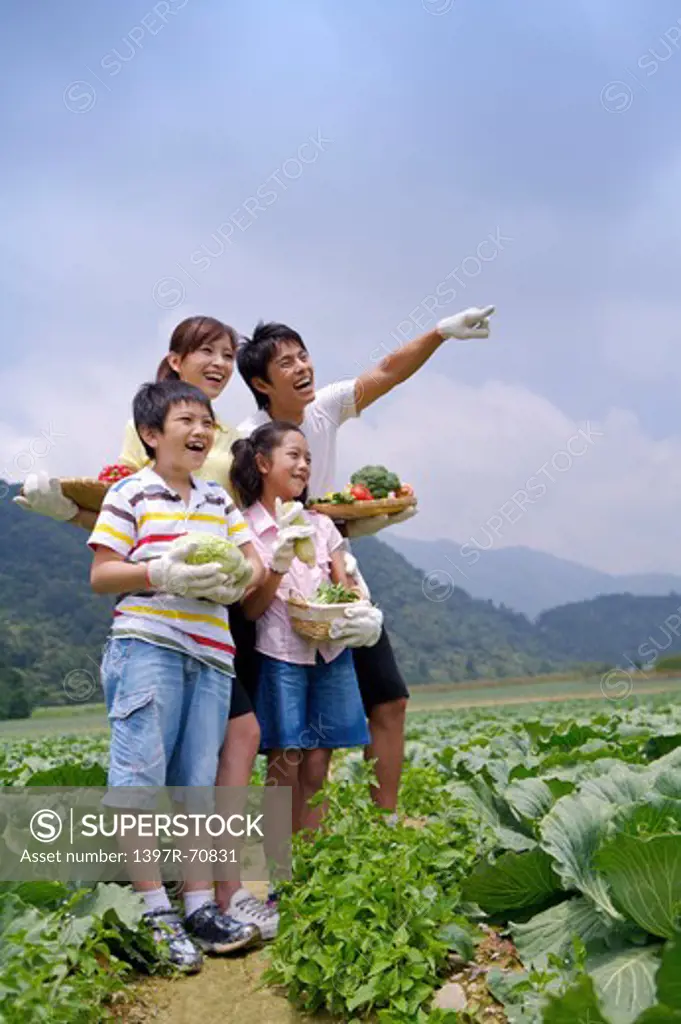 Young family with two children holding vegetables and looking away with smile