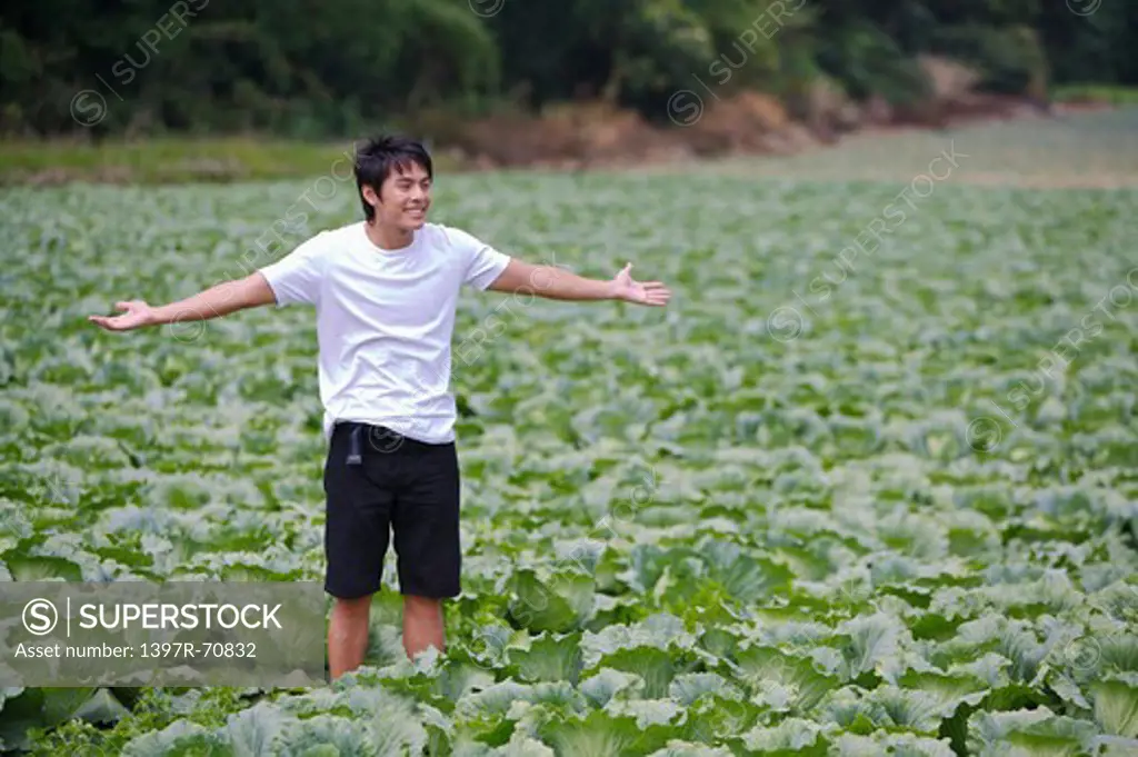Young man standing in the vegetable garden with arms outstretched and smiling