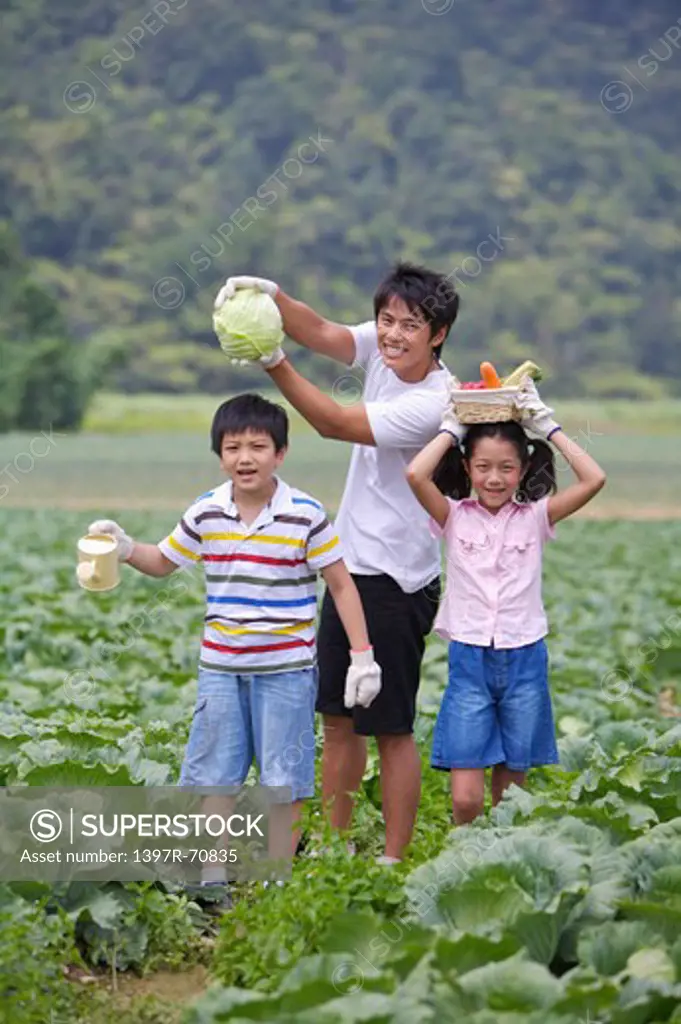 Young man with two children standing in the vegetables garden with vegetable