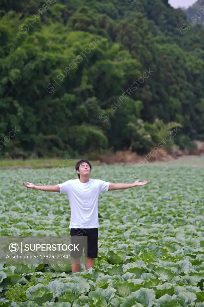 Young man standing in the vegetable garden with arms outstretched and deep breathing