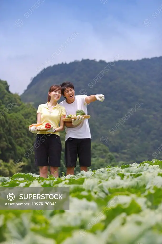 Young couple holding vegetables and looking away with smile