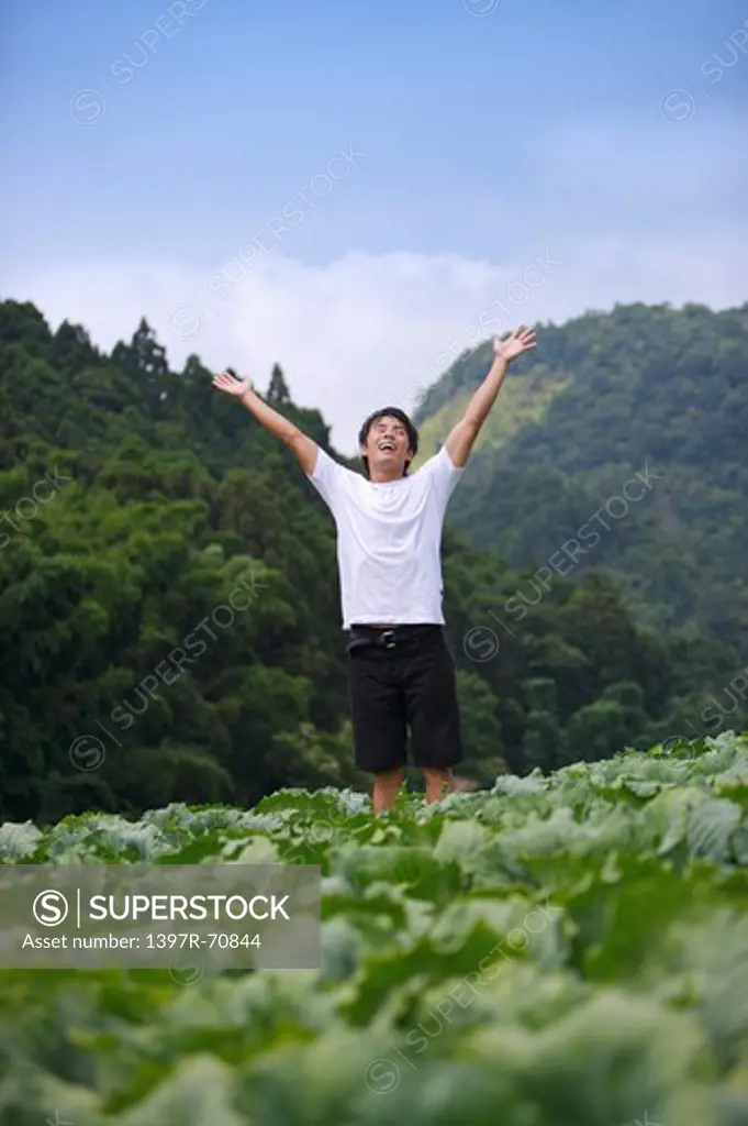 Young man standing in the vegetable garden with arms outstretched
