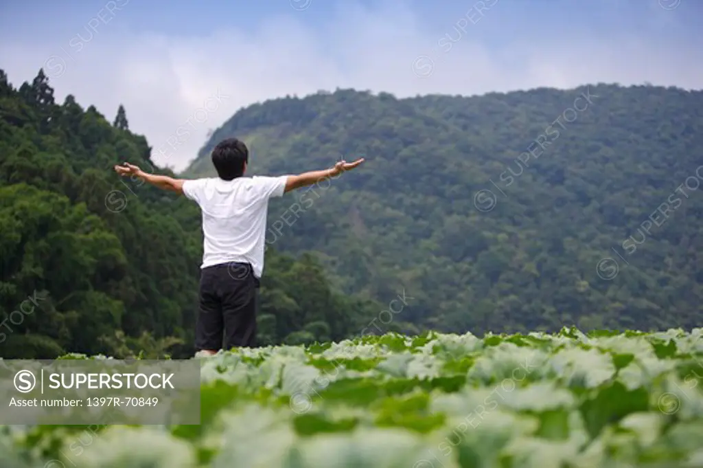 Young man standing in the vegetable garden with arms outstretched