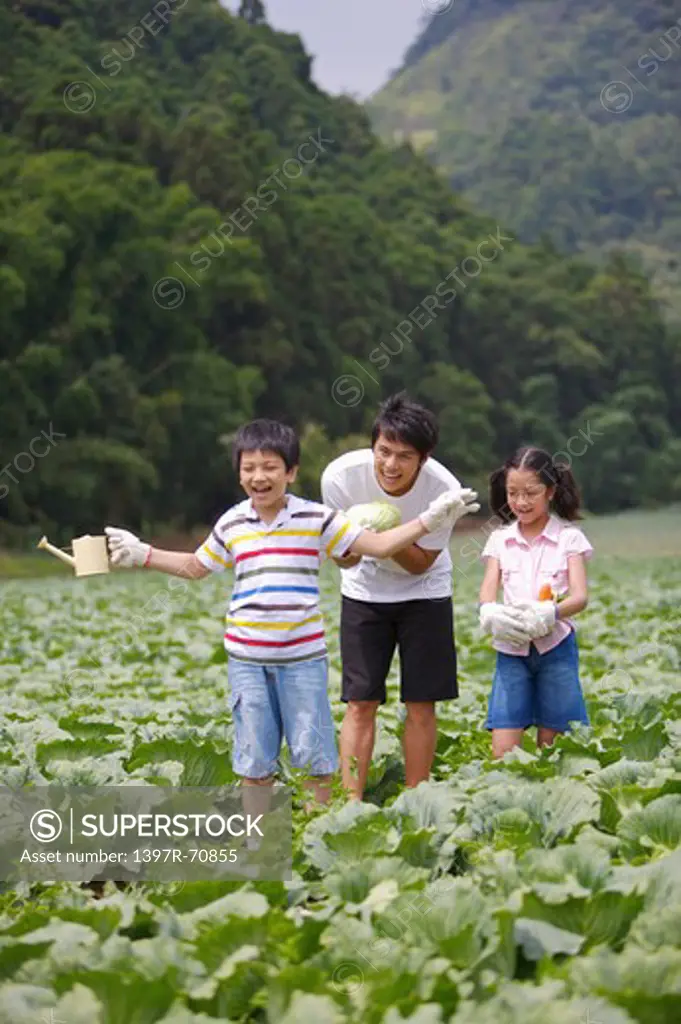 Young man with two children standing in the vegetable garden and smiling