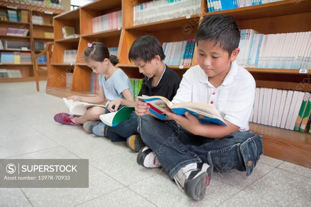 Three children sitting on the floor and reading books in the library