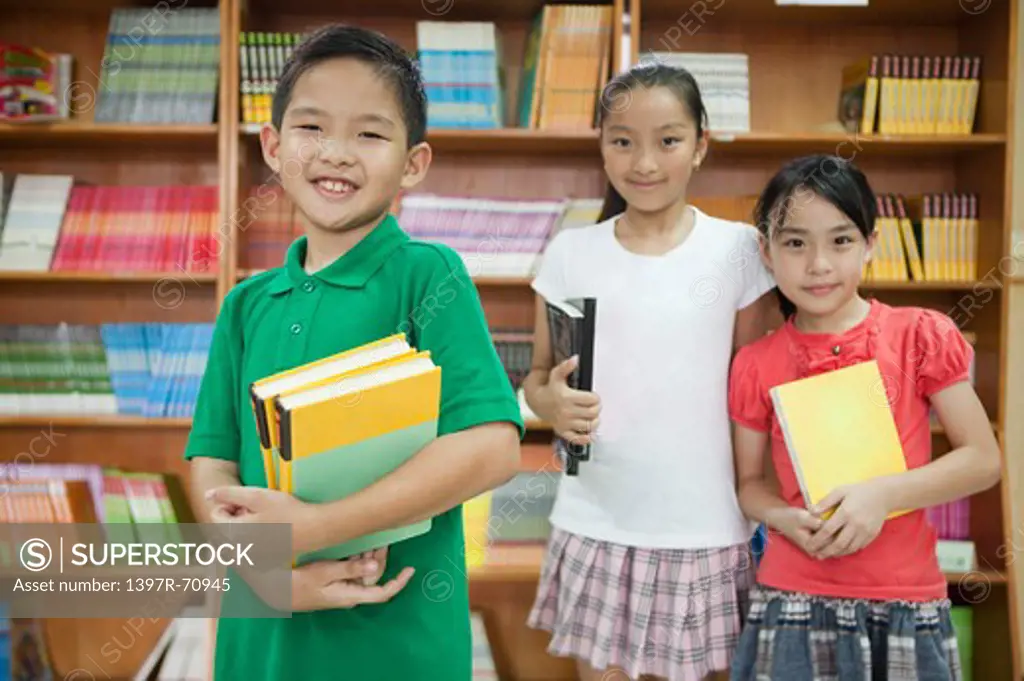 Three children standing in the library and holding books