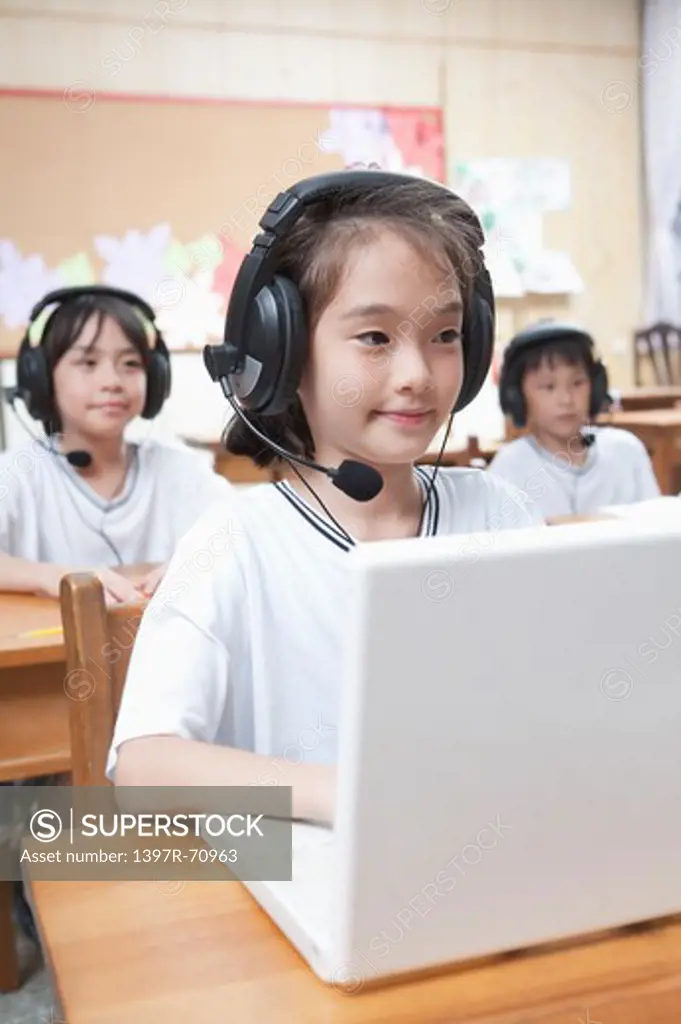 Three children studying with laptop and headphone in the classroom
