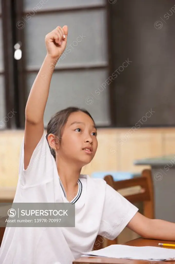 Girl sitting in the classroom with hands raised