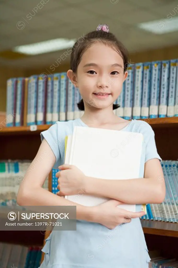 Girl holding books in the library and smiling at the camera