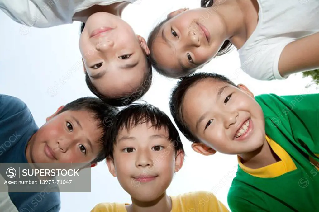 Five children looking down at camera head to head in a circle, smiling