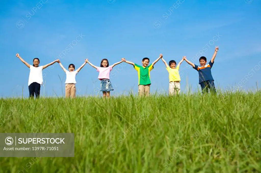Group of children standing on lawn holding raised hands