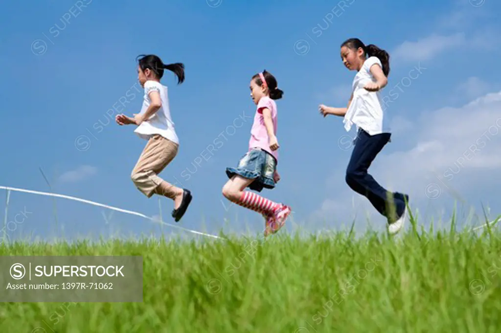 Three girls skipping over rope on lawn