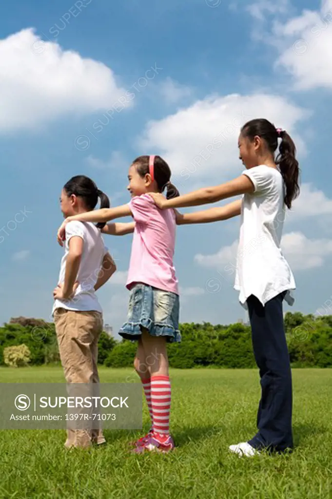 Three girls standing in a row on lawn, hands on shoulders