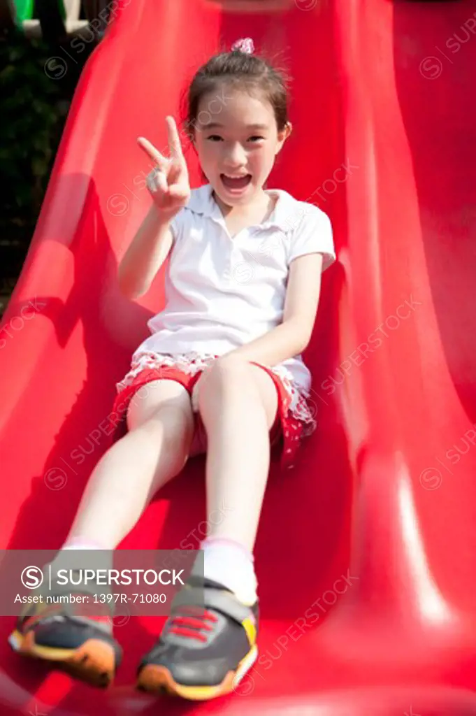 Girl sitting on slide giving peace sign