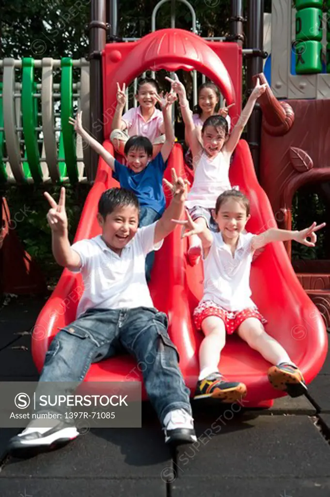 Group of children sitting on slide, giving peace sign