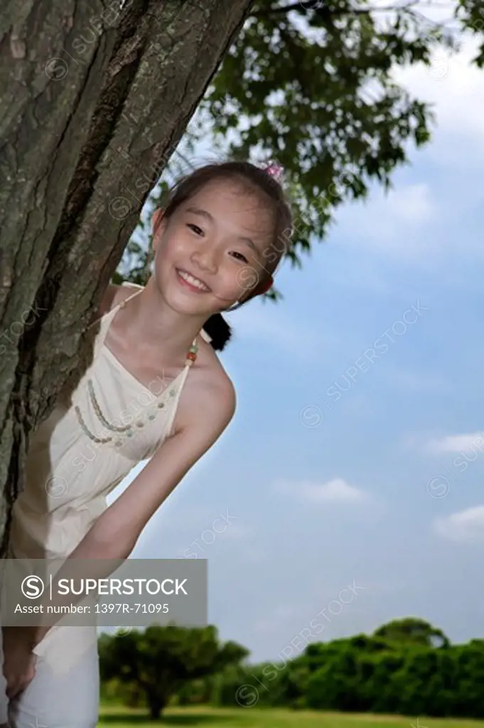 Girl smiling from behind a tree trunk