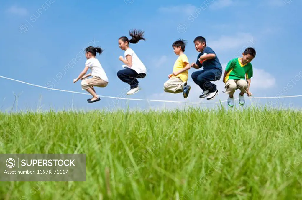 Group of children skipping over rope on grass