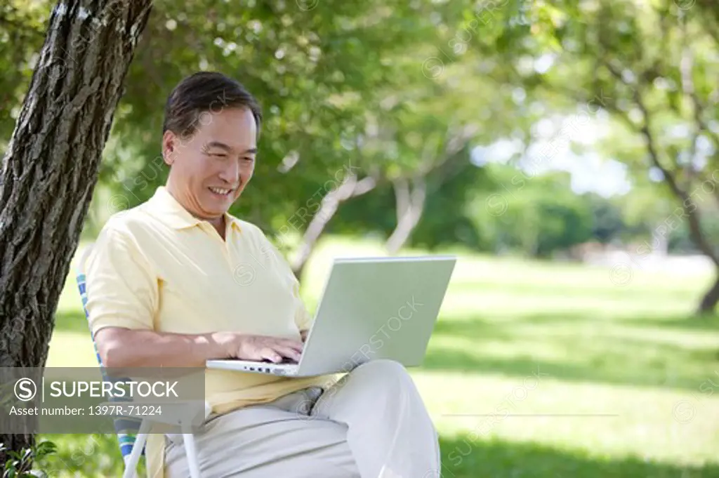 Senior man sitting in a park with a laptop