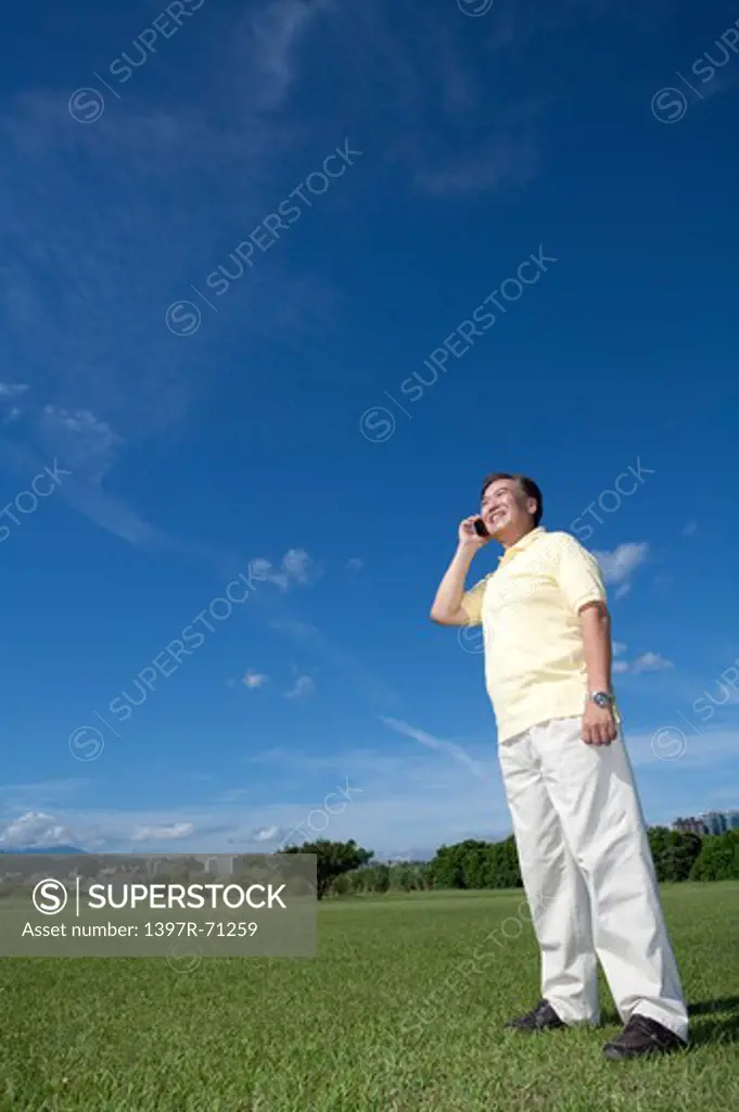 Senior man standing on lawn and talking on cell phone