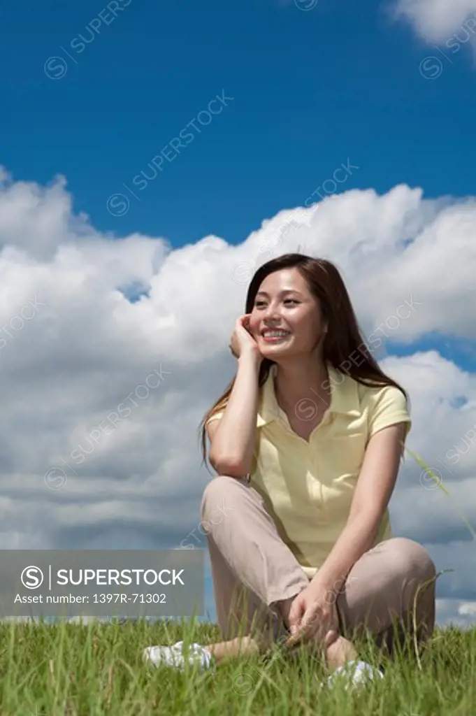 Young woman sitting on grass and looking away with smile
