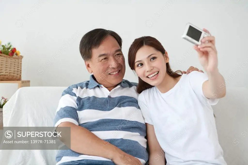 Father and daughter sitting on sofa and taking picture with smile
