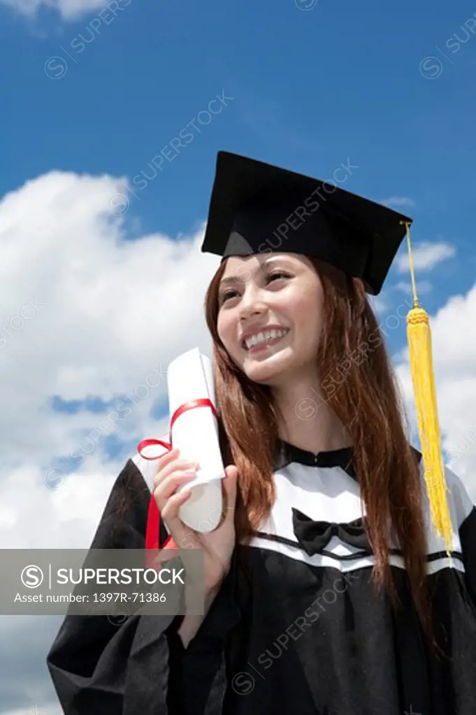 Young woman holding diploma and looking away with smile on graduation