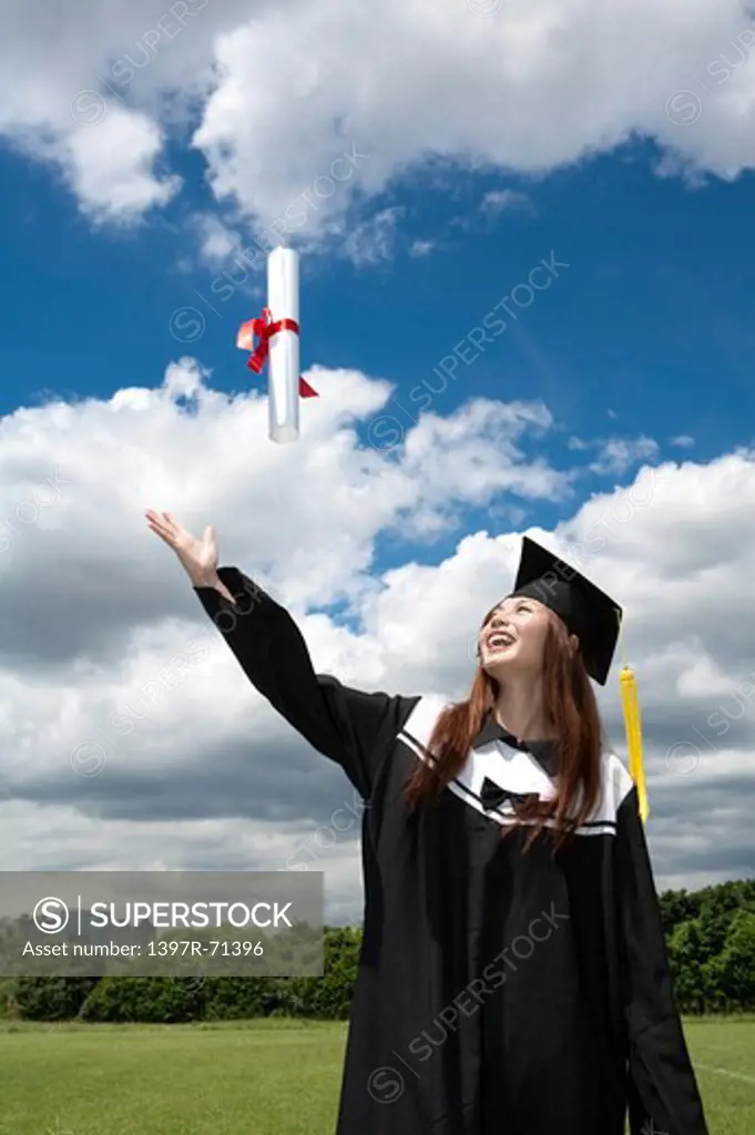 Young woman looking up with arm outstretched and smiling on graduation