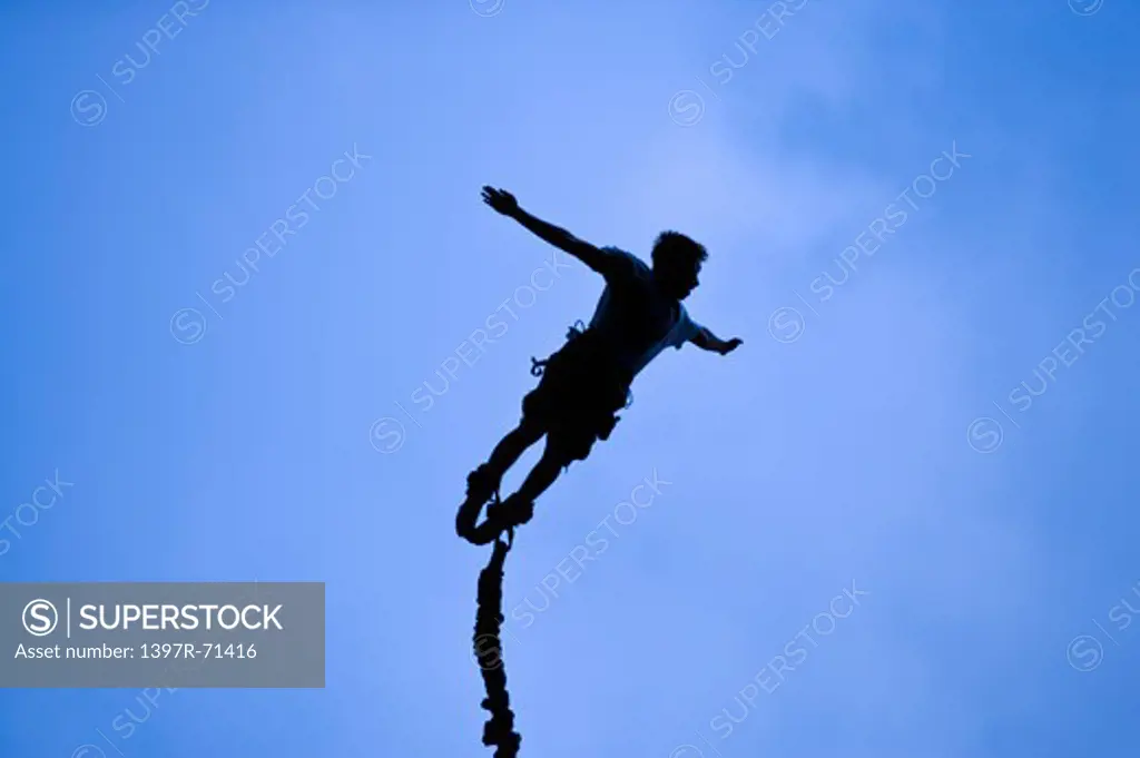Bungee jumper silhouetted against sky, low angle view