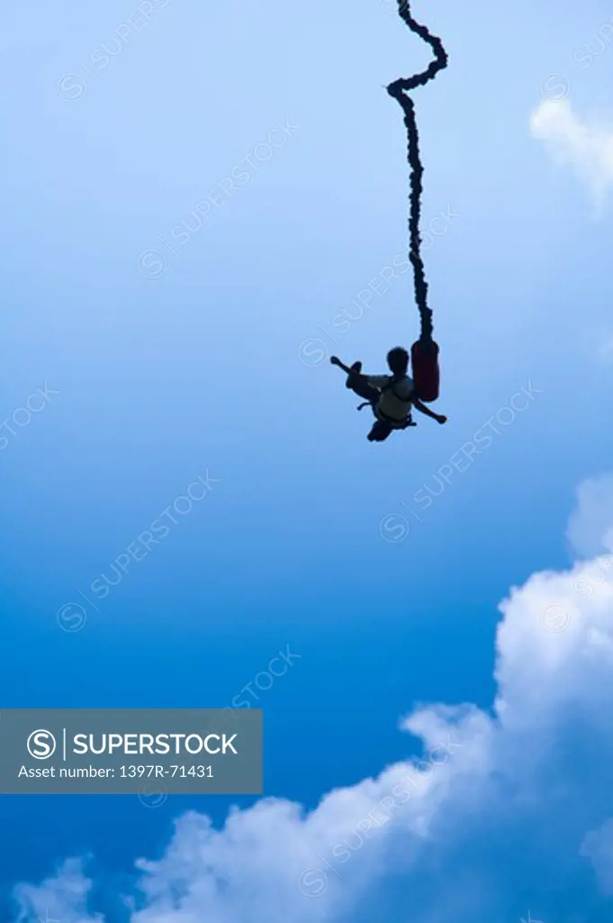 Bungee jumper silhouetted against sky, low angle view