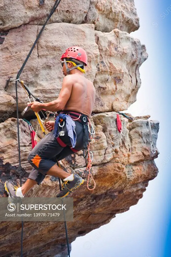 Male rock climber abseiling down cliff face