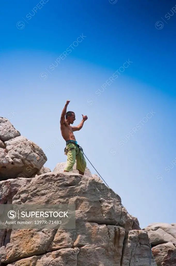 Male climber standing on mountain peak with arms up celebrating his success