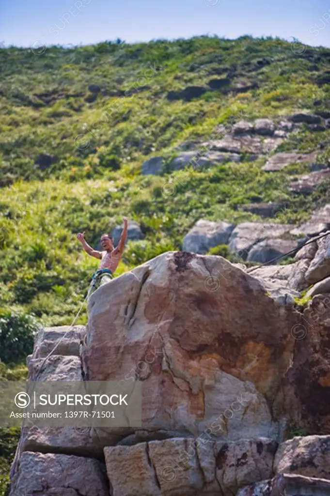 Male climber standing on top of a rock with arms up celebrating his success