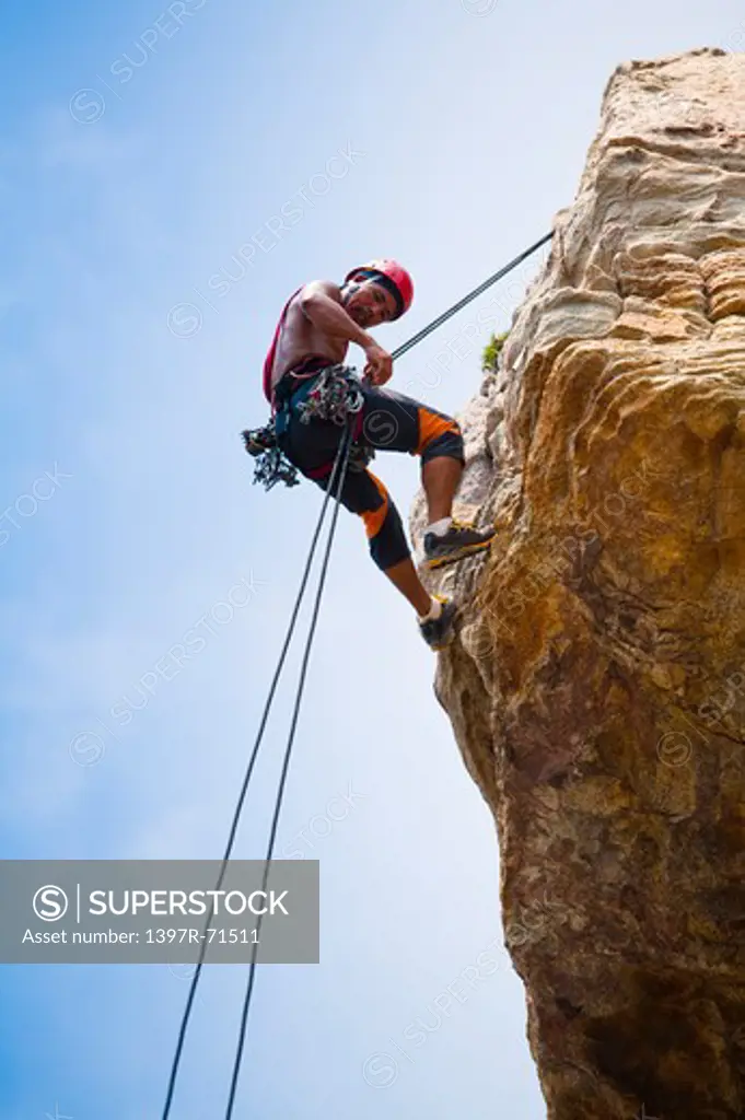 Male rock climber abseiling down cliff face