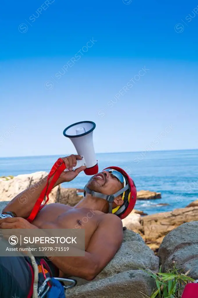 Male rock climber lying on rocks and talking through megaphone