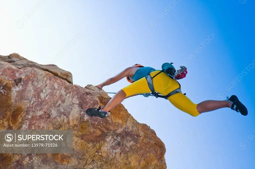 Woman rock climbing on cliffs, low angle view