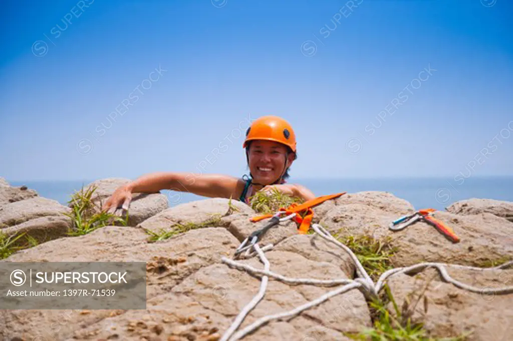 Female rock climber arriving at the top of cliff, smiling