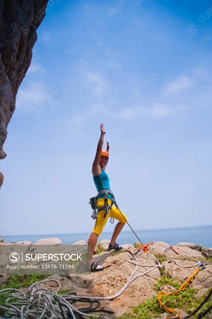 Female rock climber standing on rock with arms up